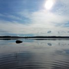 Tranquil sunrise scene: lake, clouds, trees, boat, surreal rocks