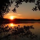 Colorful sunset over lake with person, ducks, and autumn leaves