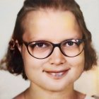 Young girl with curly hair wearing glasses and colorful paint splatters on her face