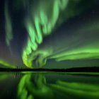 Vivid green aurora borealis and UFO over calm waters