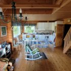 Sunlit cozy room with wooden beams, plants, rocking chairs, and bookshelf.