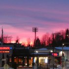 Twilight scene: Cozy log cabins, tall pine trees, starry sky, vibrant sunset