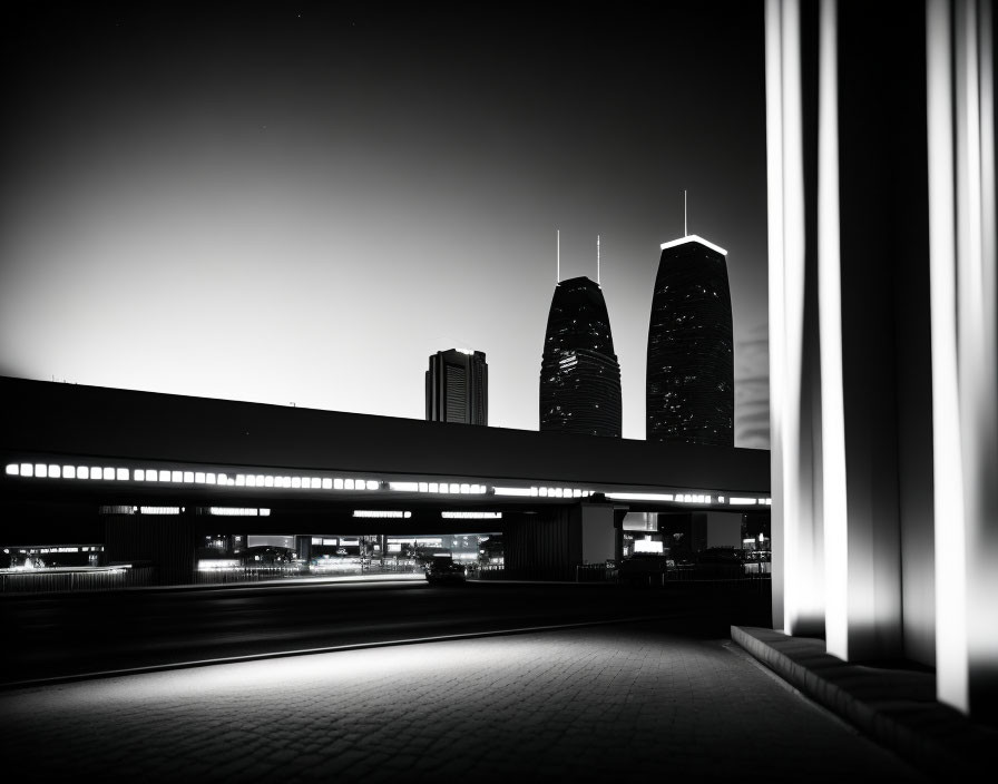 Monochrome cityscape: night scene with lit skyscrapers, overpass, and vertical lights.