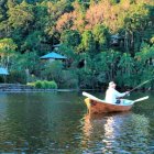 Tranquil painting of person fishing in red and white boat on calm waters