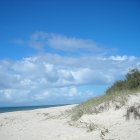 Serene beach watercolor painting with blue sky, boats, and dune