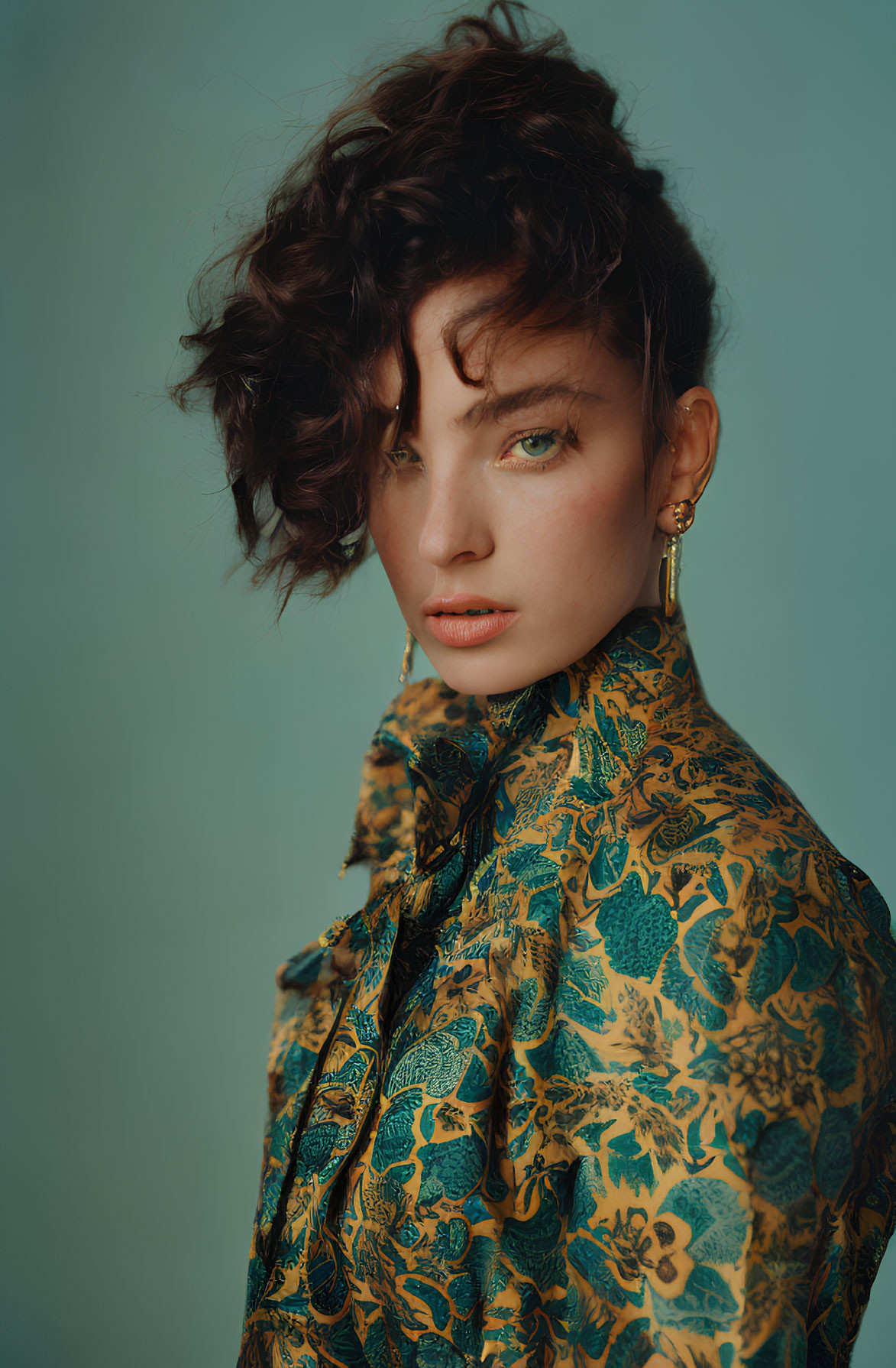 Woman with Short Curly Hair and Green Eyes in Patterned Blouse on Teal Background