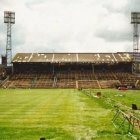 Deserted stadium with green field, floodlights, and cloudy sky.