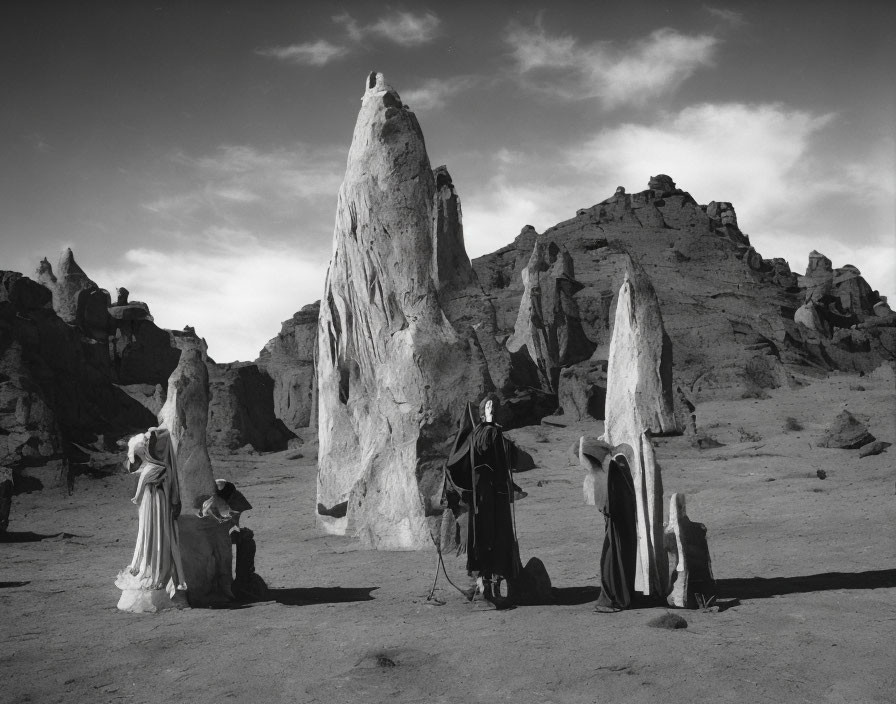 Monochrome photo: Three robed figures in rocky landscape