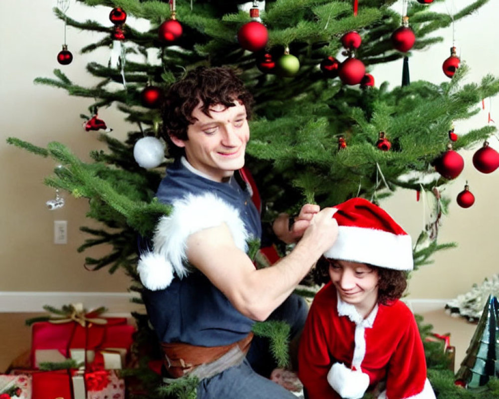 Man and child in Santa hats decorate Christmas tree with presents