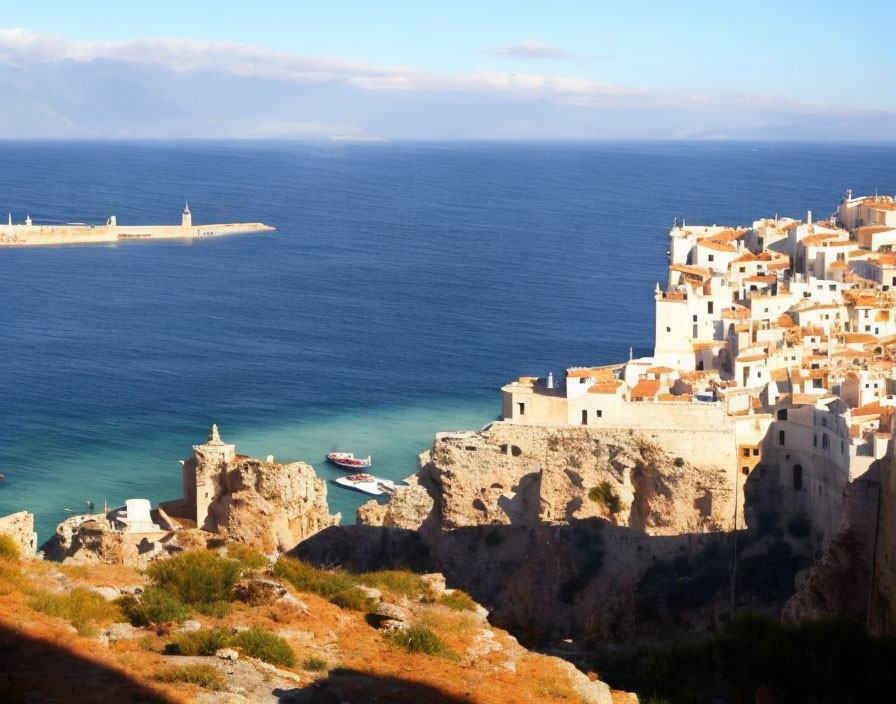 Picturesque Coastal Town with White Buildings, Blue Sea, Boat, and Ruins