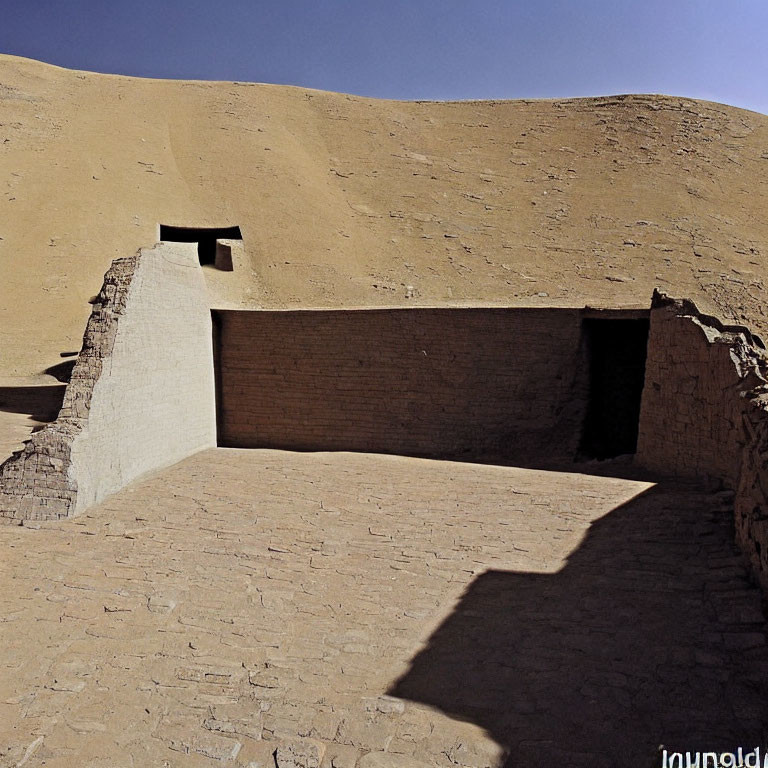 Ancient adobe ruins in desert with small rectangular opening and contrasting shadows