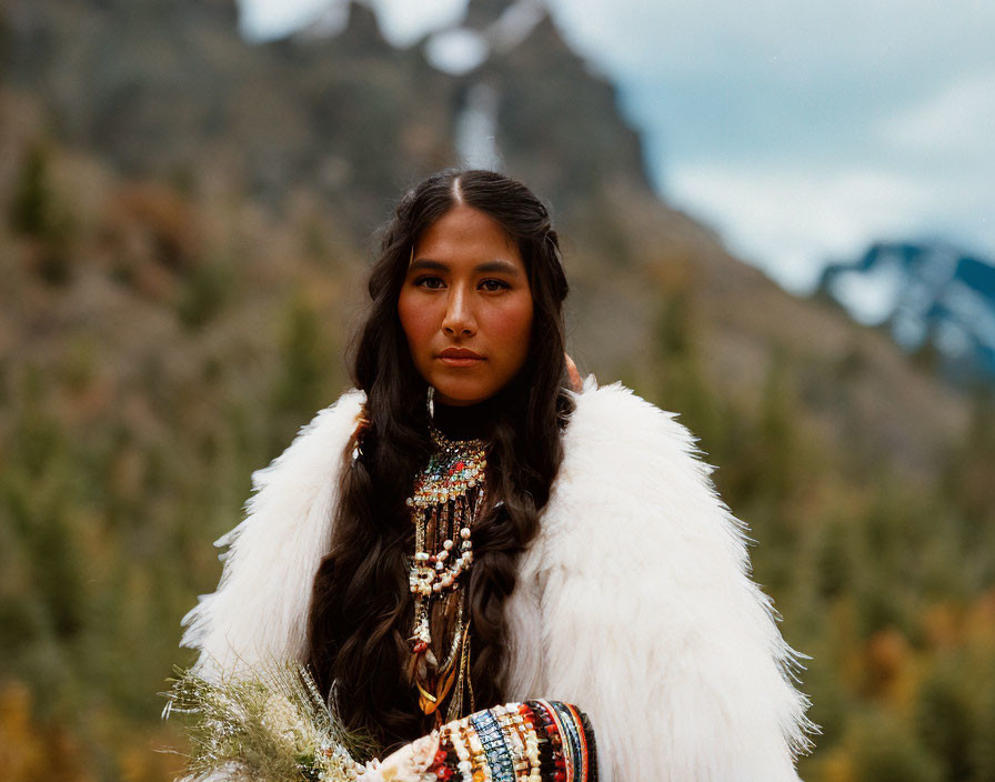 Indigenous woman in traditional attire with beadwork against mountain backdrop