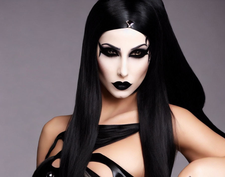 Dramatic black and white makeup with long black hair and dark attire on grey background