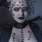 Bald person with dramatic makeup and jewels in high-collared black outfit