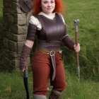 Female warrior fantasy figurine with red hair, brown leather armor, gauntlets, and crescent