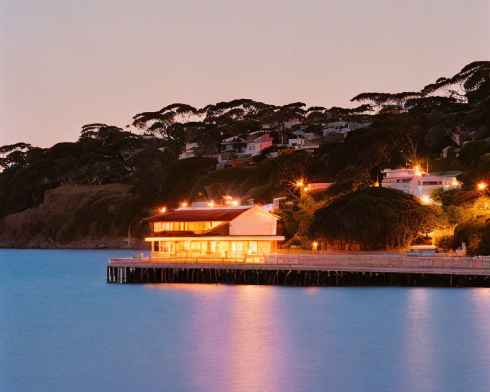 Twilight scene with warmly lit building on pier & silhouetted trees