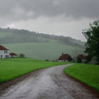 Rural landscape with mist, dirt road, farmhouses, hills, crop, and tree