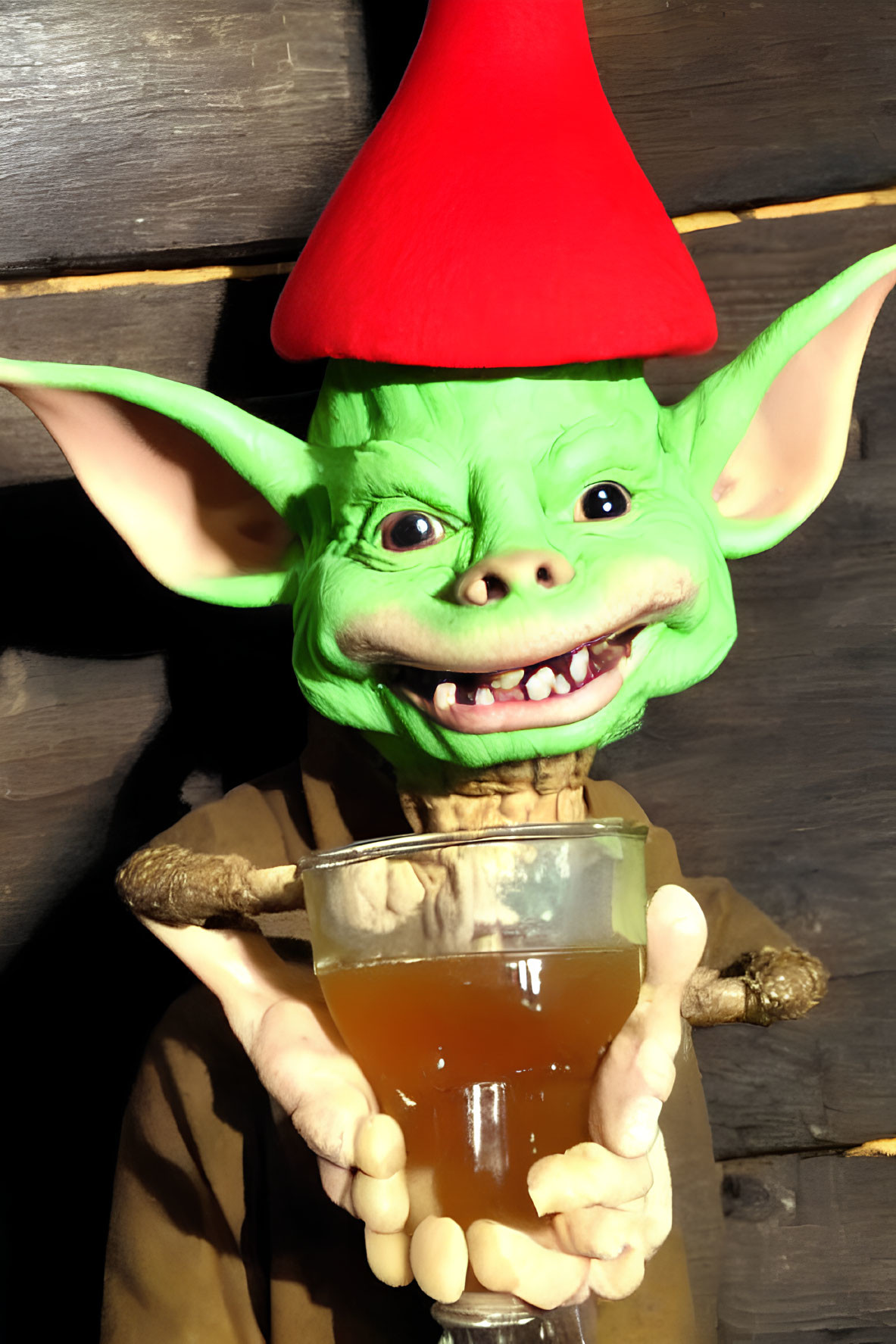 Green goblin with pointy ears and red hat holding a golden-brown drink