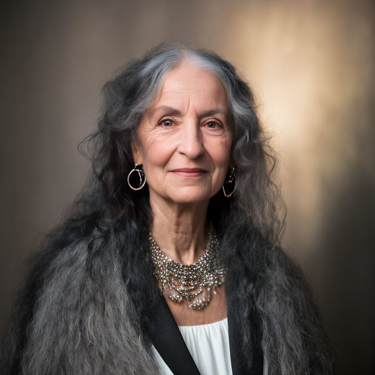 Elderly woman with gray hair and earrings smiling in white blouse and necklace