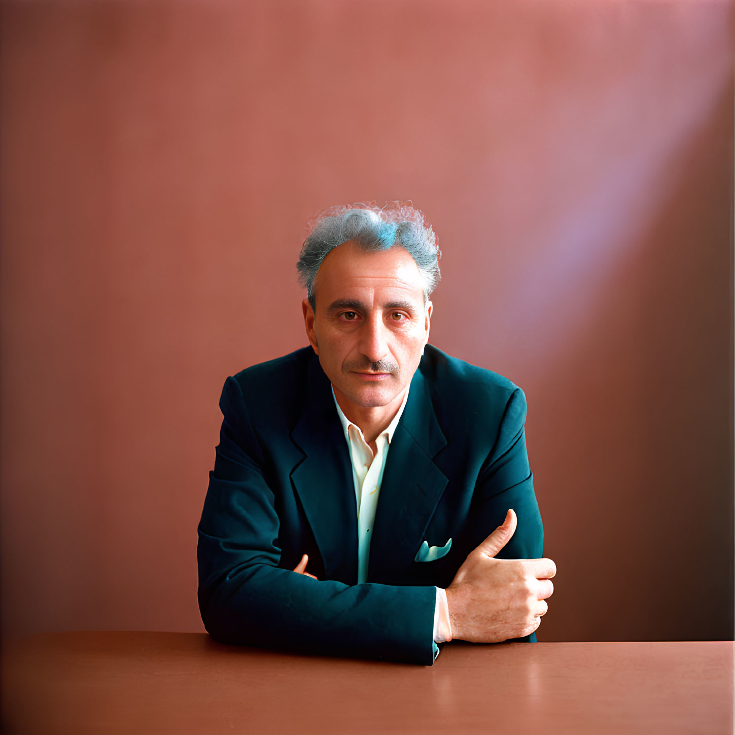 Salt-and-Pepper-Haired Man in Dark Suit and Green Shirt Seated Against Maroon Back