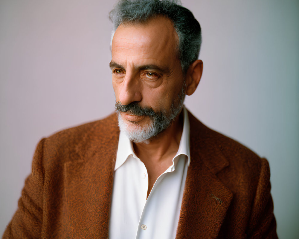 Elderly man with salt-and-pepper hair in white shirt and rust-colored jacket gazes thought