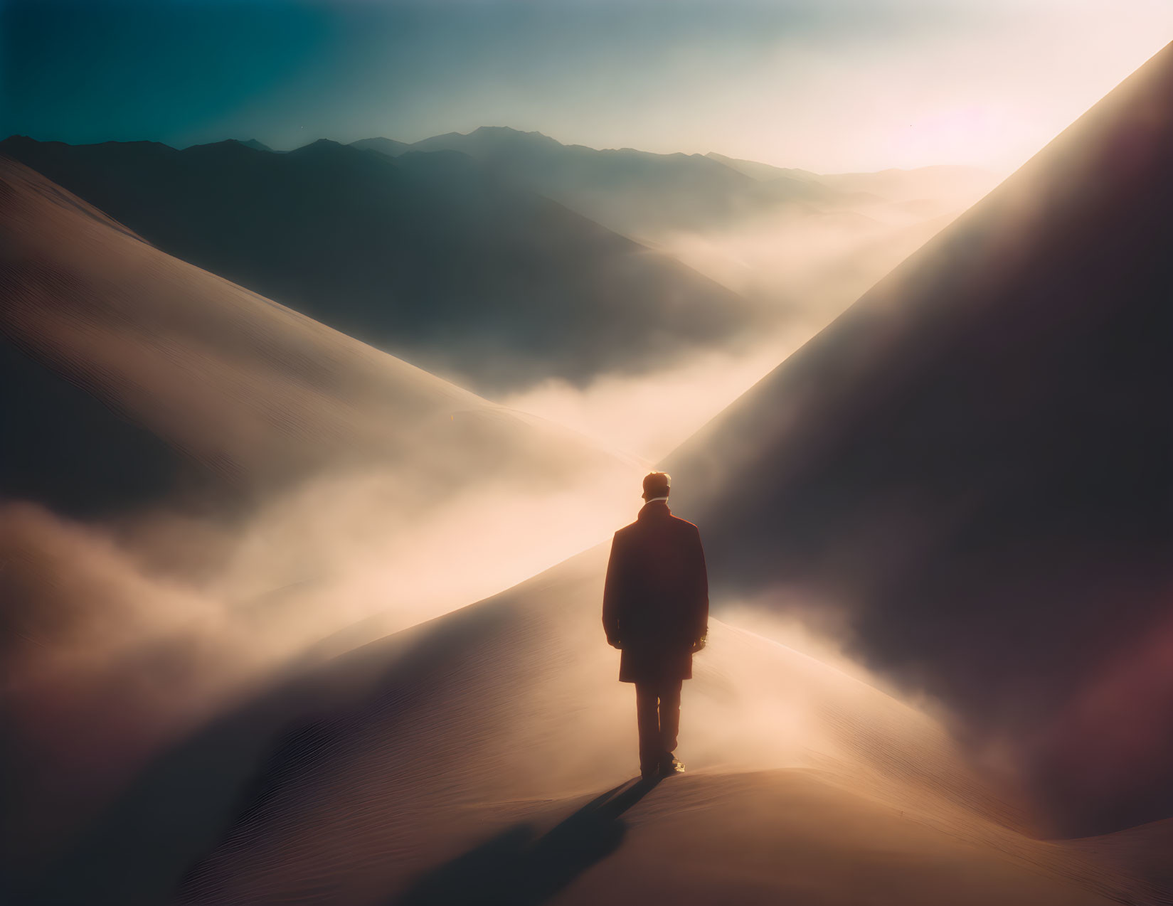 Solitary figure on sand dune at sunrise with misty hills.