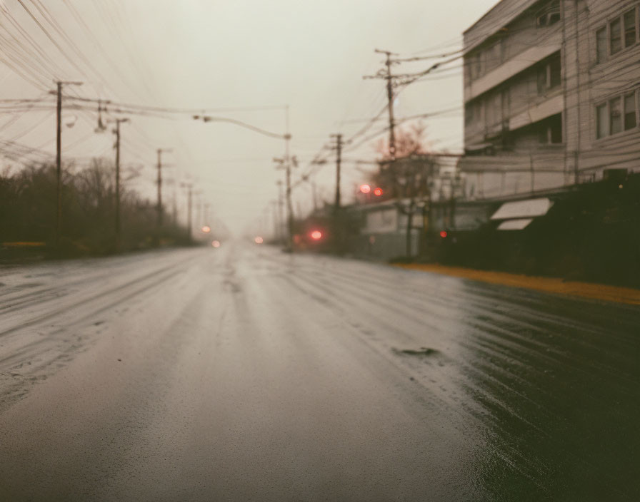 Urban scene: Rainy street with reflective asphalt, traffic lights, vehicles, and utility wires in mist