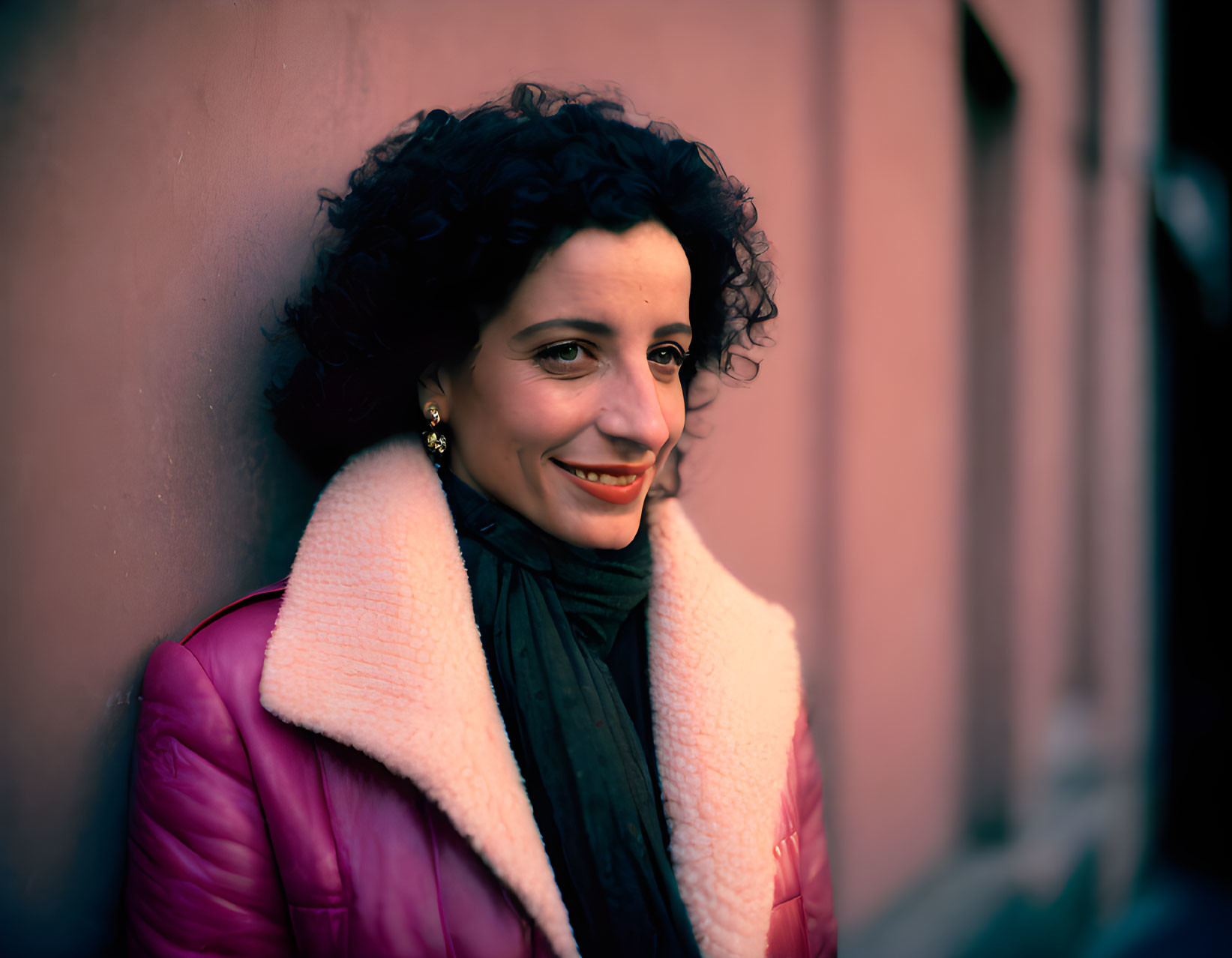 Curly-Haired Woman Smiling in Pink Jacket on Pink Background