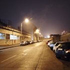 Snowy night scene: dimly lit street with parked cars, glowing streetlight, and foggy