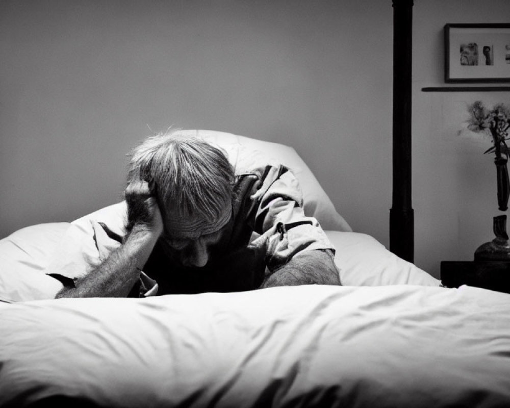 Elderly person in distress on bed in black and white