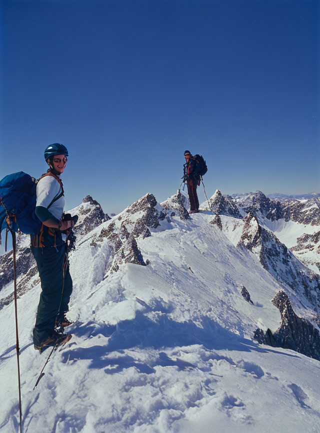 Climbers with backpacks and safety gear on snowy mountain ridge