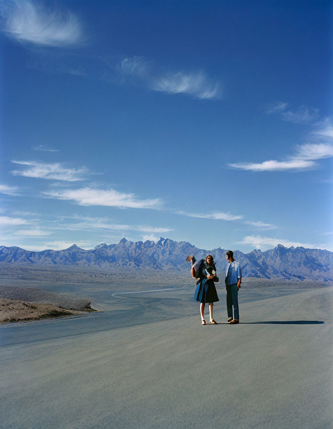 Three People on Barren Landscape with Clear Sky & Distant Mountains