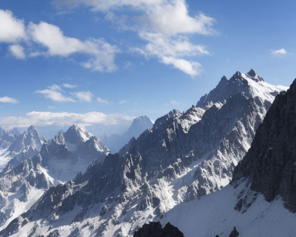 Scenic snow-covered mountain peaks under blue sky with scattered clouds