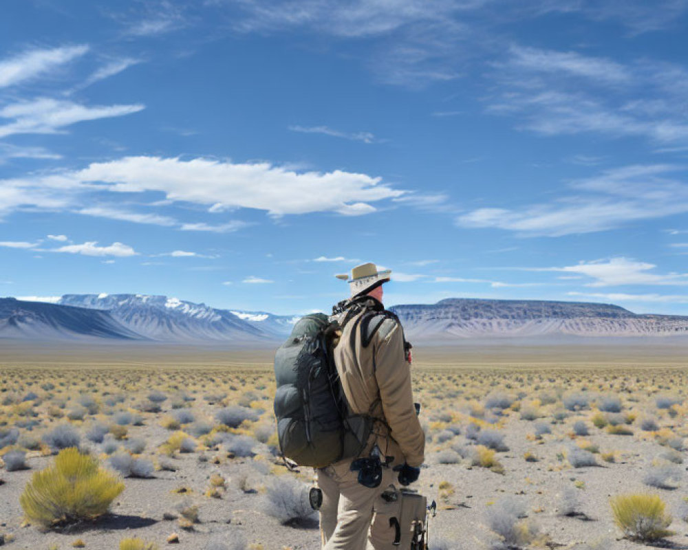 Traveler with large backpack and camera in desert landscape with mountains.