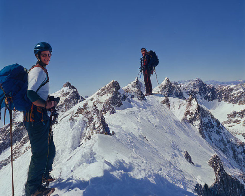 Climbers with backpacks and safety gear on snowy mountain ridge