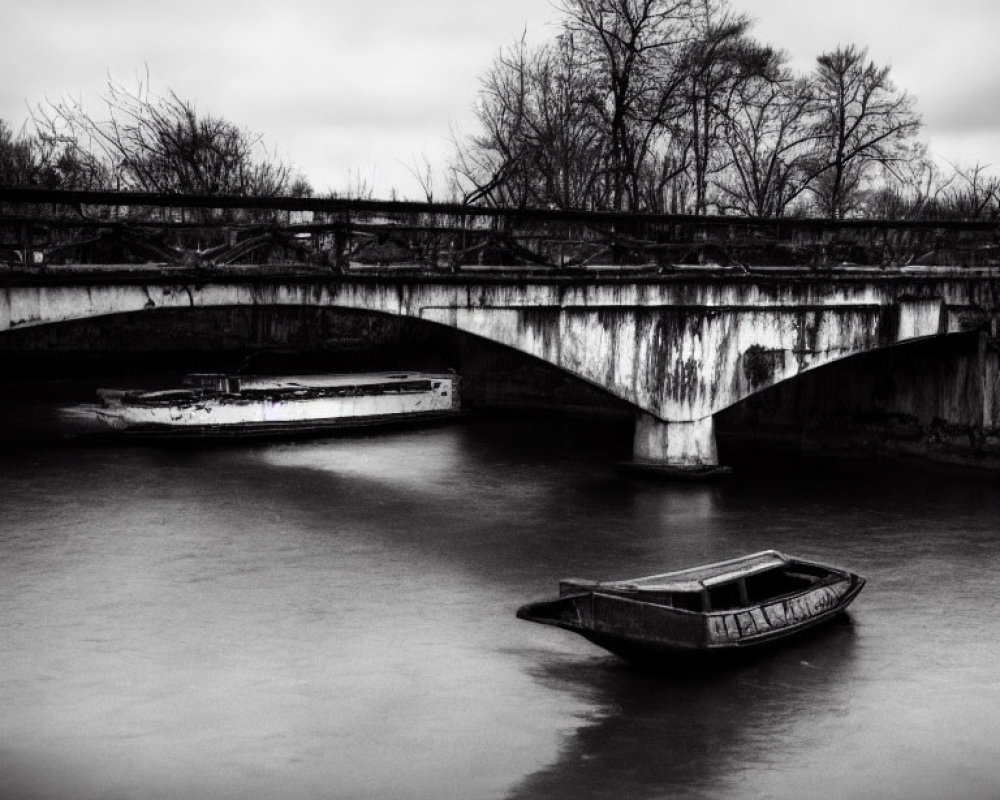 Serene river scene with old bridge, abandoned boats, and barren trees