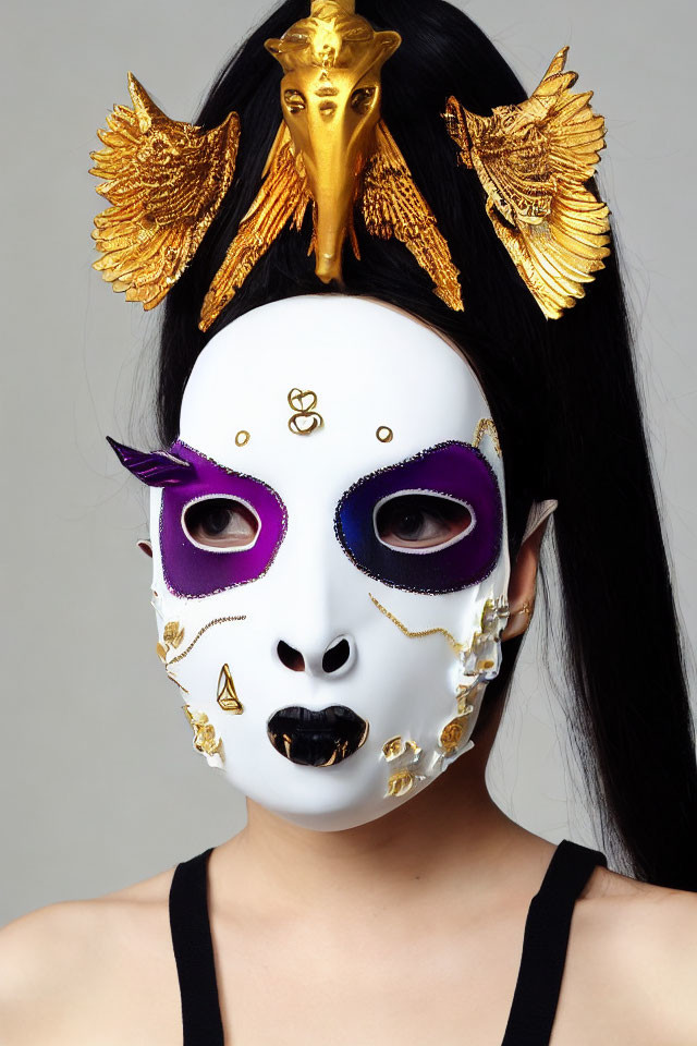 Dark-haired person in white mask with purple, gold, and wings