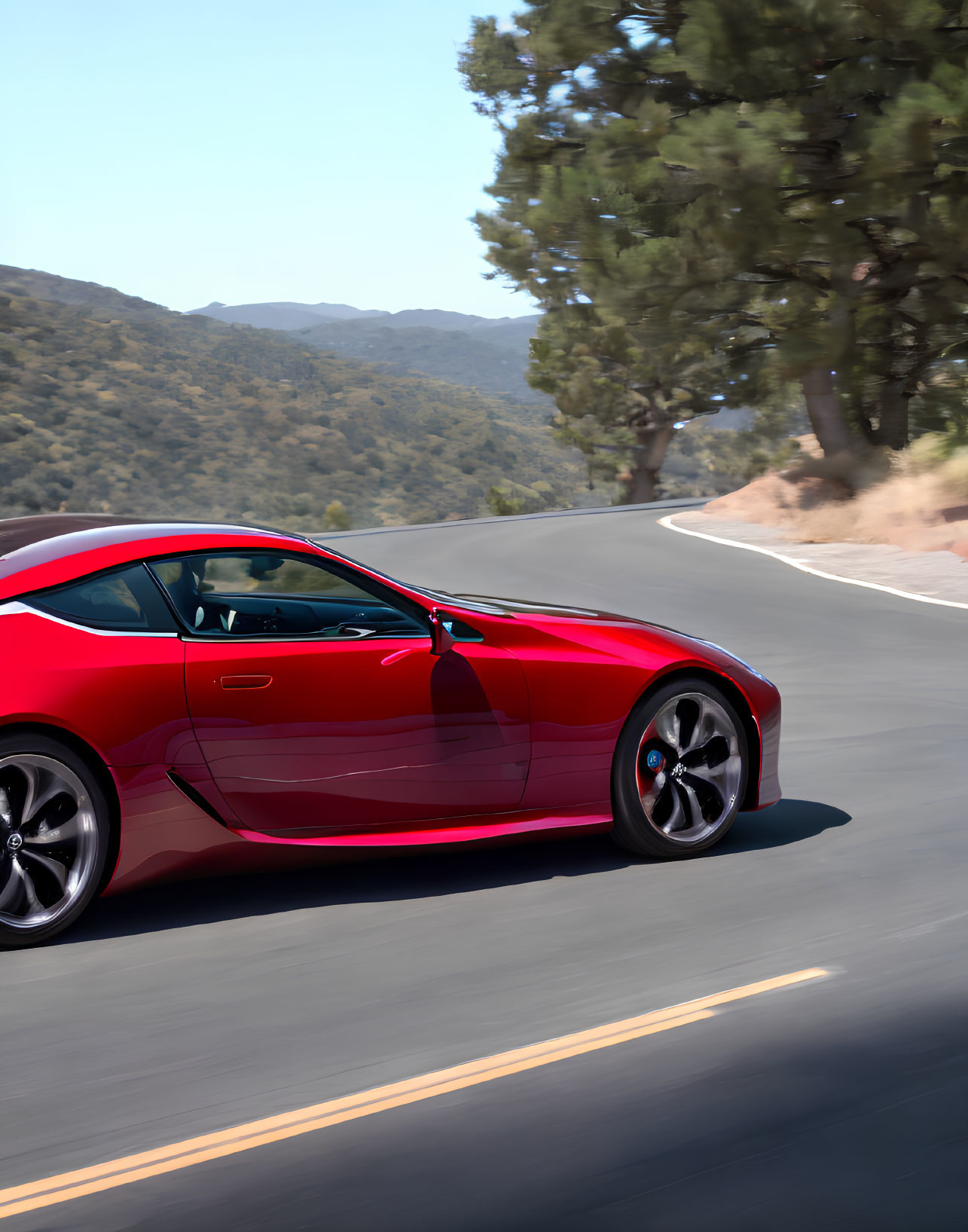 Red sports car on road under clear blue skies with lush greenery