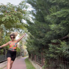 Joyful woman in black outfit running towards floating bubbles on path with trees and fence.