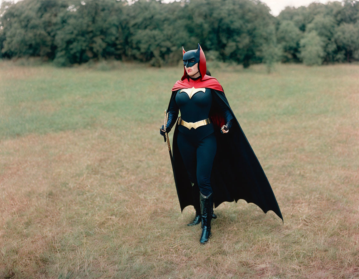 Cosplayer in Batgirl costume with cape and utility belt in grassy field