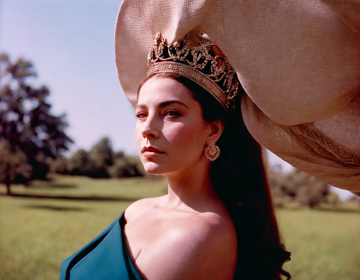 Woman in crown and large hat posing outdoors with trees and clear sky.