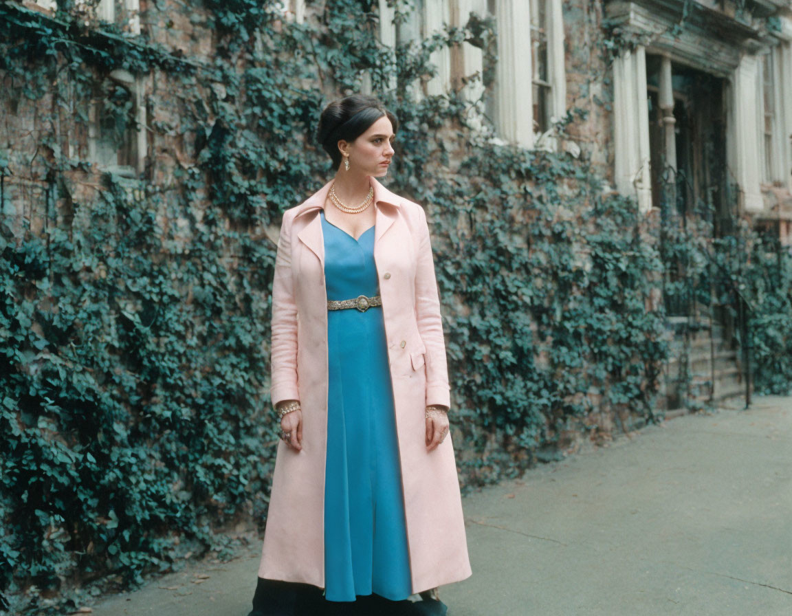 Woman in Blue Dress and Pink Coat Poses in Front of Ivy-Covered Building