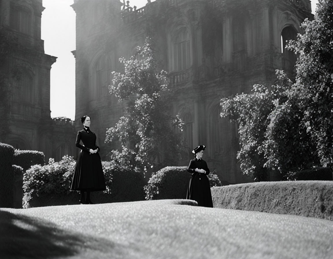 Vintage-dressed women in sculpted garden with grand building in black and white.