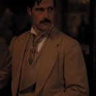 Dapper man with mustache in tan trench coat and pocket watch on dark backdrop