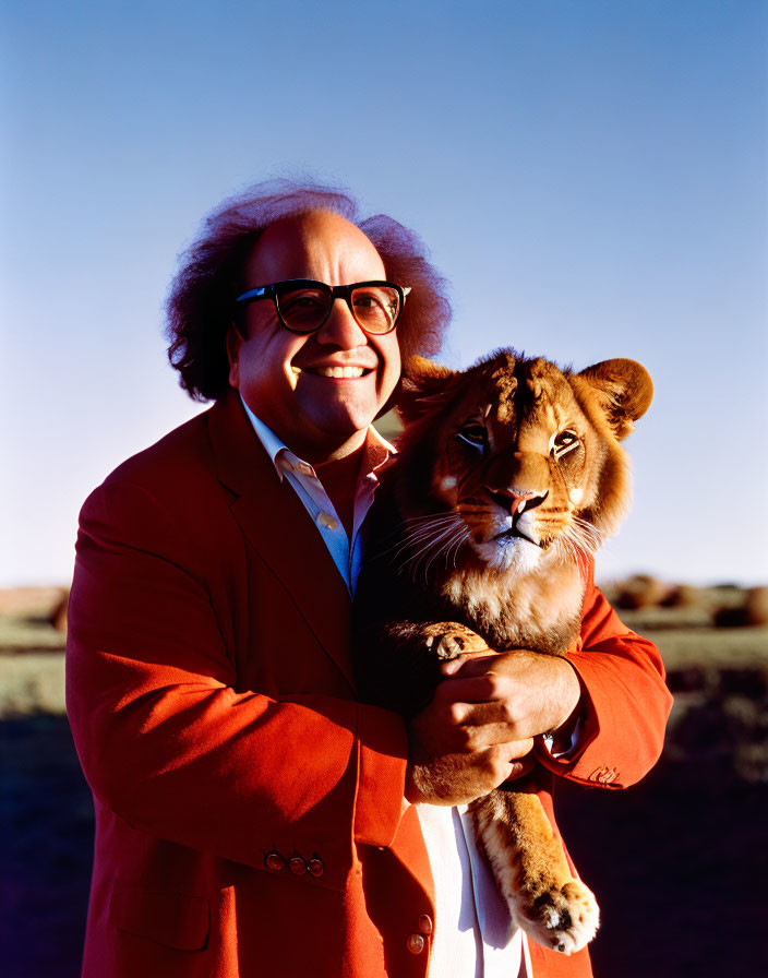 Man in large glasses holds lion cub in sunny outdoor scene