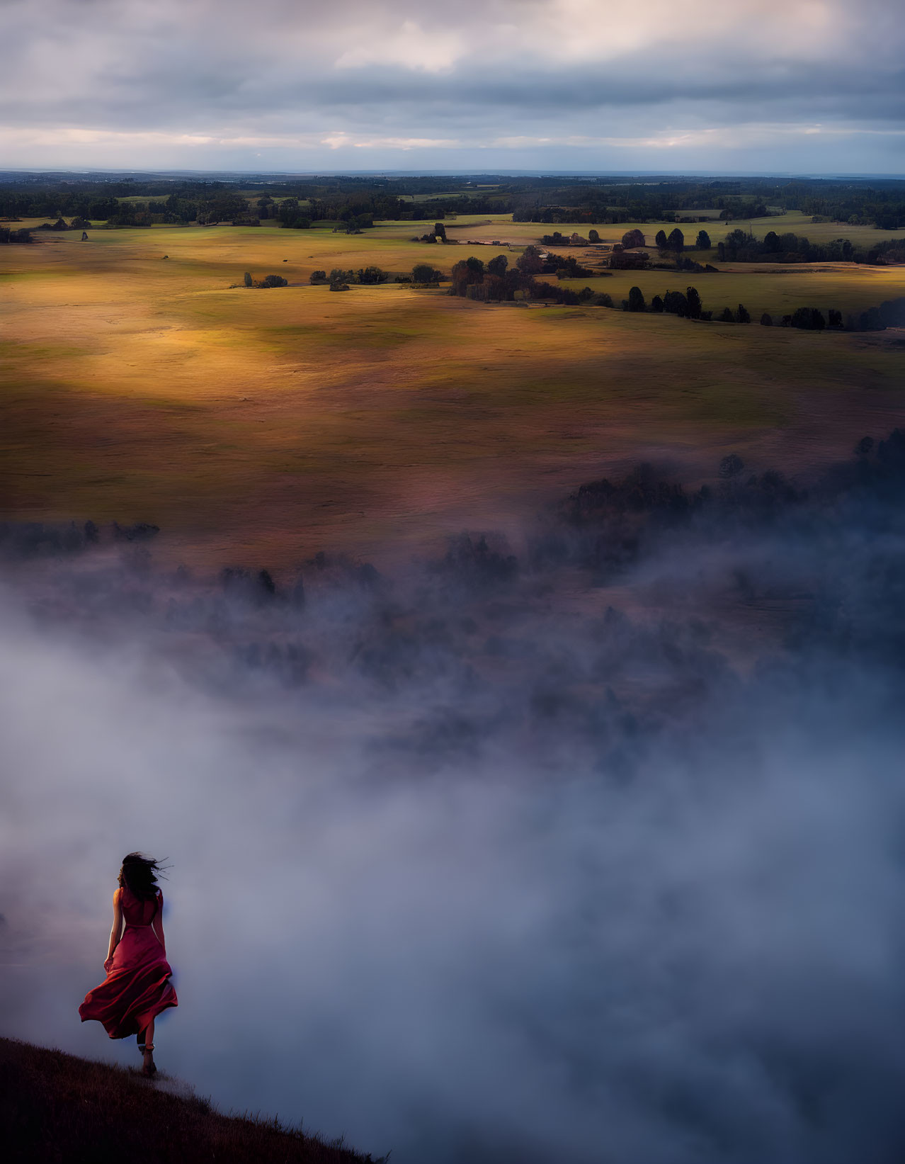 Person in red dress on hill overlooking misty valley at dusk