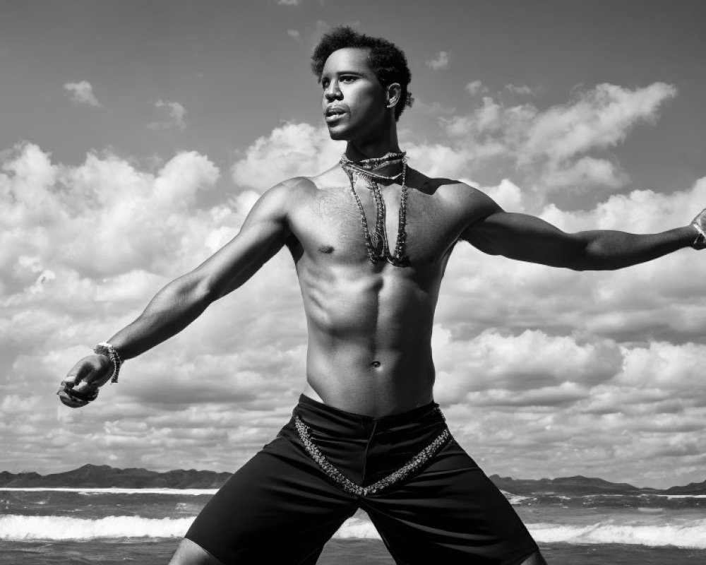 Toned shirtless man on beach with outstretched arms