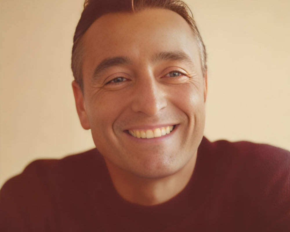 Smiling man with short hair in burgundy shirt on beige background