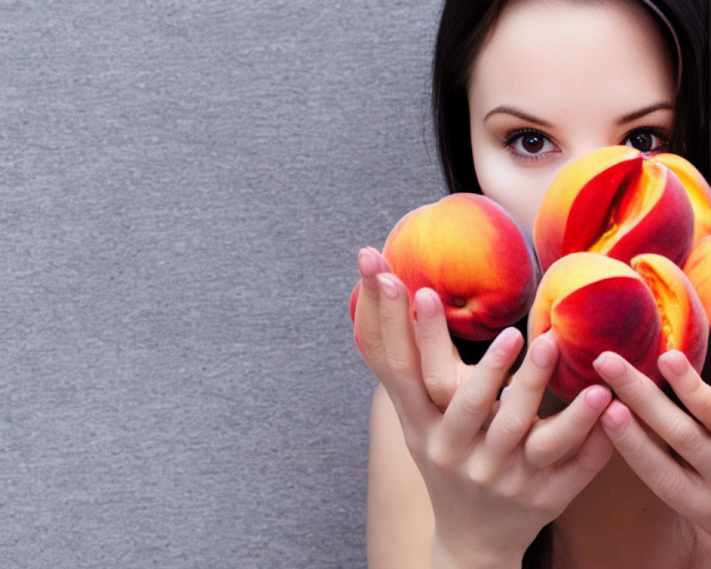 Person holding ripe peaches near face on grey background