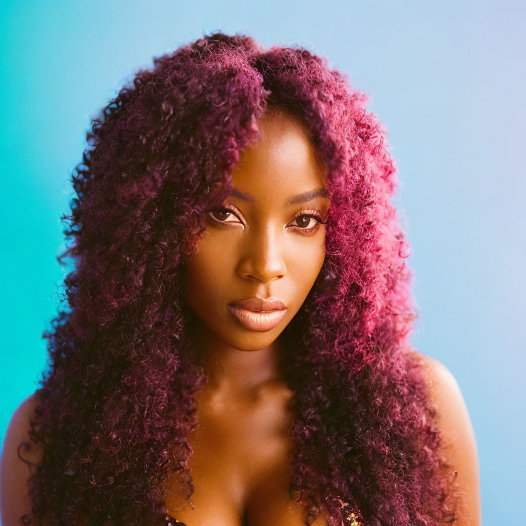 Portrait of woman with curly magenta hair against blue backdrop